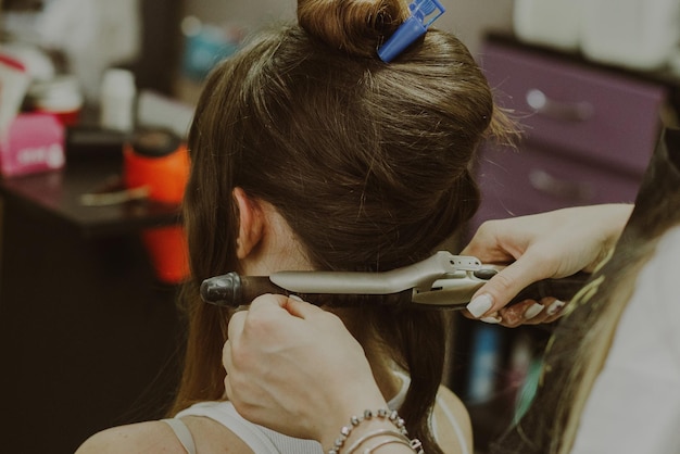 Ragazza ritratto seduta in un negozio di parrucchiere con un maestro che le torce i capelli su un ferro da stiro