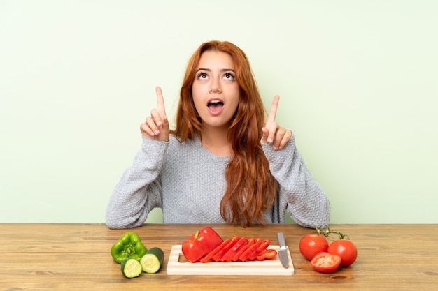 Ragazza rossa adolescente con verdure in una tabella che punta con il dito indice una grande idea