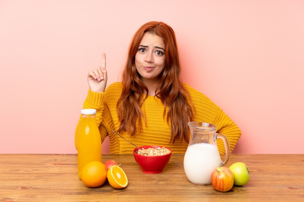 Ragazza rossa adolescente facendo colazione in una tabella che indica con il dito indice una grande idea