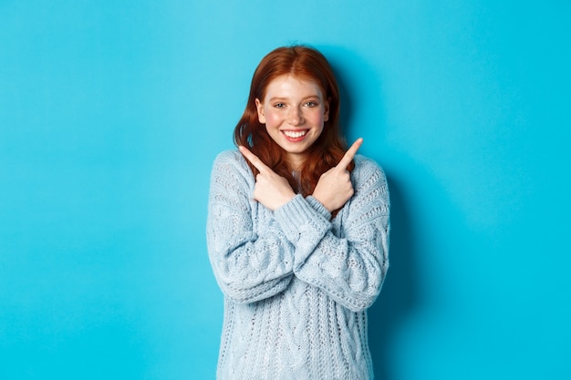 Ragazza rossa allegra che mostra due scelte, indicando lateralmente e sorridendo su sfondo blu. Copia spazio