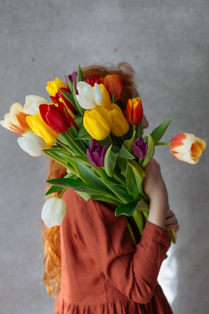 Ragazza rossa che tiene un mazzo di tulipani multicolori.