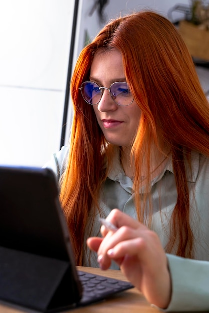 Ragazza rossa con gli occhiali che lavora con il tablet