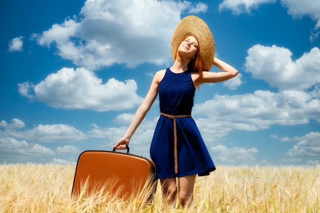 Ragazza rossa con la valigia al campo di grano primaverile.