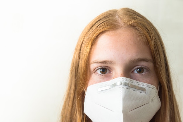 Ragazza rossa con maschera bianca, guardando dritto nella telecamera con spazio vuoto a sinistra dell'immagine e sfondo bianco