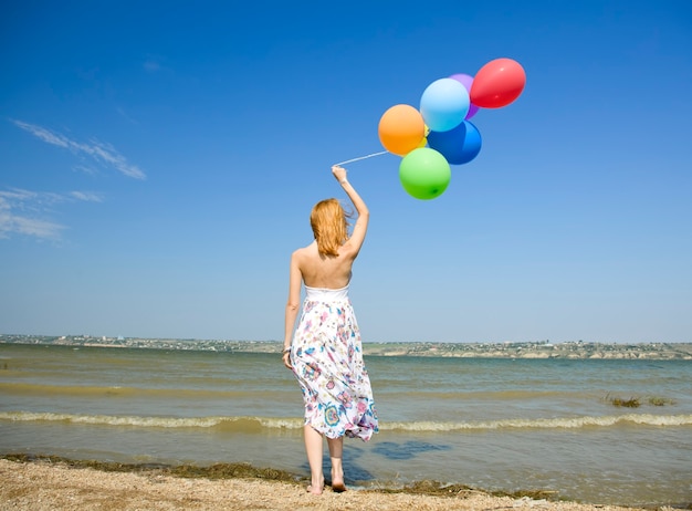 Ragazza rossa con palloncini di colore al litorale.