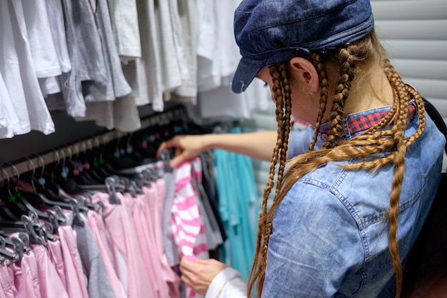 Ragazza rossa con taglio di capelli treccia scegliendo abiti in un negozio