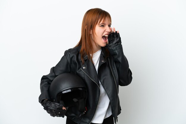 Ragazza rossa con un casco da motociclista isolato su sfondo bianco che grida con la bocca spalancata di lato