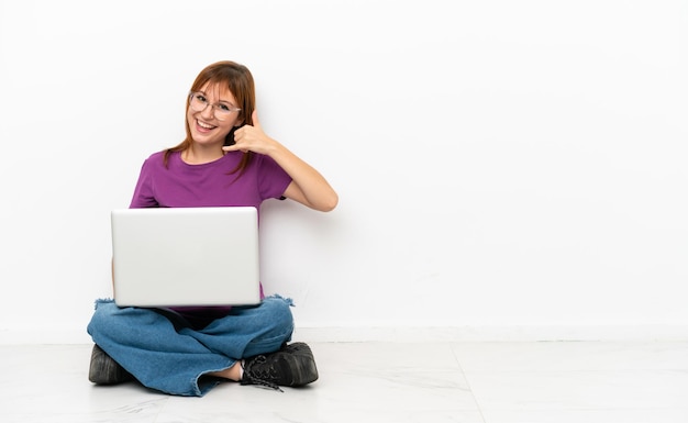 Ragazza rossa con un laptop seduto sul pavimento che fa un gesto telefonico Chiamami indietro segno