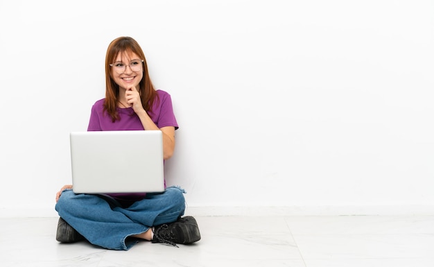 Ragazza rossa con un laptop seduto sul pavimento che guarda di lato e sorride