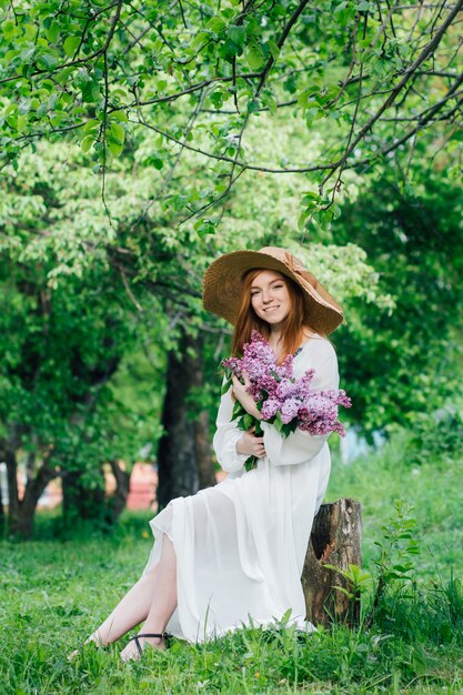 Ragazza rossa con un mazzo di lillà in un giardino di primavera