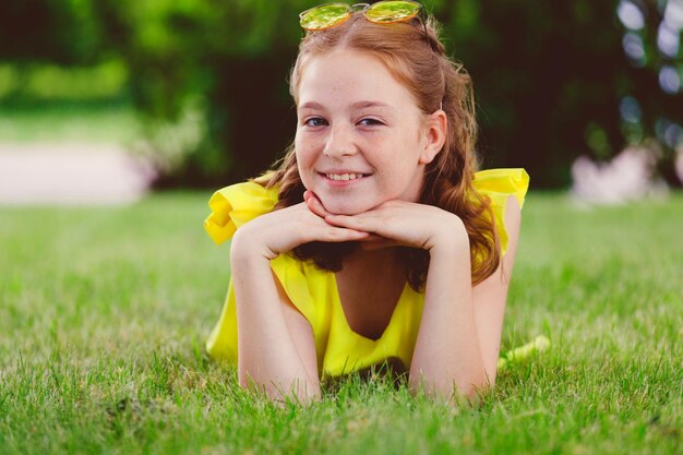 Ragazza rossa in un vestito giallo sull'erba nel parco in estate Foto di alta qualità