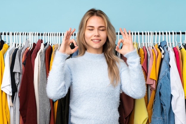 Ragazza russa che compra alcuni vestiti sulla parete blu nella posa di zen