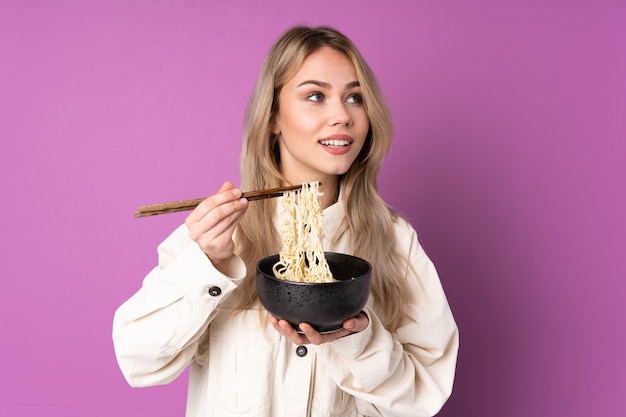 Ragazza russa dell'adolescente isolata sulla porpora che tiene una ciotola di tagliatelle con le bacchette e che osserva in su