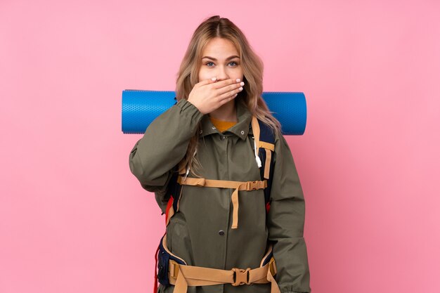 Ragazza russa dell'alpinista dell'adolescente con un grande zaino sulla bocca rosa del rivestimento murale con le mani