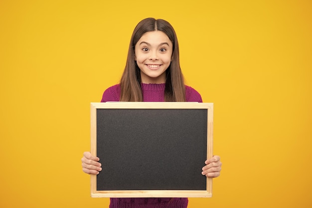 Ragazza scolarica adolescente che tiene la lavagna vuota della scuola isolata su sfondo giallo Ritratto di una studentessa adolescente Copia della pubblicità dello spazio