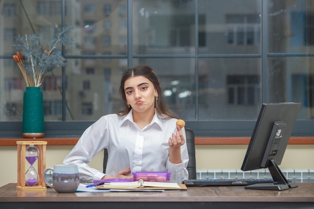 Ragazza sconvolta che tiene il biscotto fresco fatto e che esamina la macchina fotografica