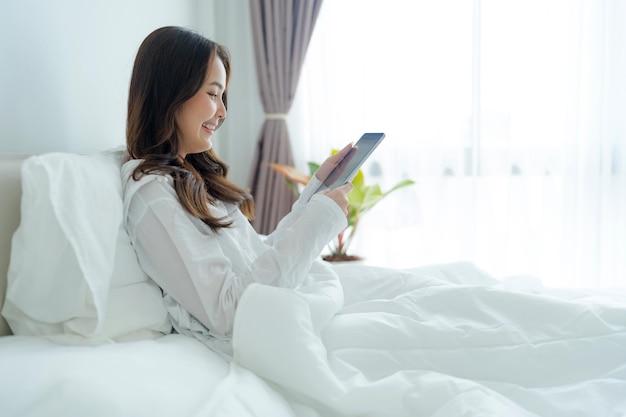 Ragazza sdraiata a letto giocando al computer tablet in camera da letto