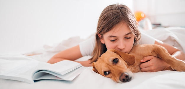 Ragazza sdraiata nel letto con il suo cane e il libro di lettura