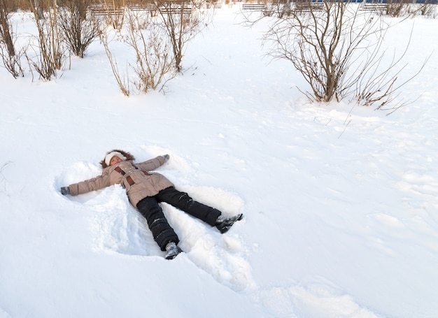 Ragazza sdraiata nella neve. Inverno nel parco cittadino.