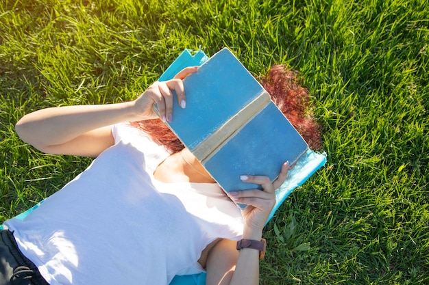 Ragazza sdraiata sul libro di lettura dell'erba