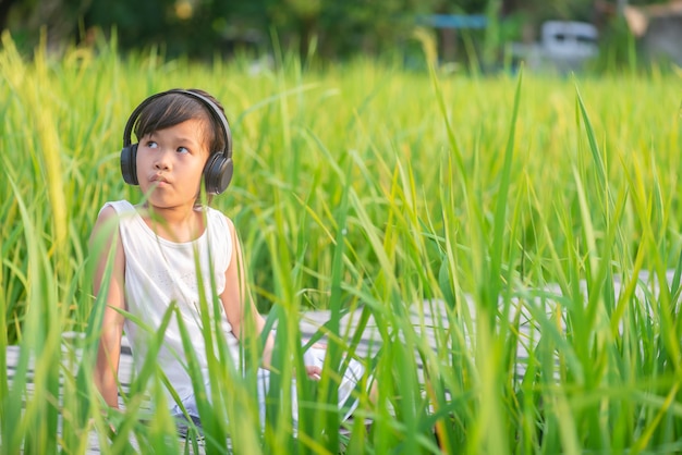 ragazza seduta e ascoltando musica sul ponte di legno nel campo di riso sul tramonto