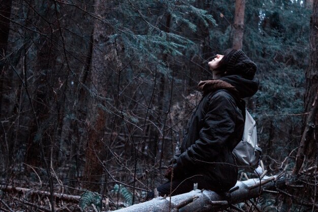 Ragazza seduta in una foresta su un albero caduto e guardando il cielo