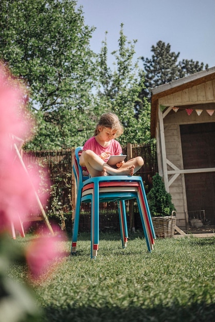 Ragazza seduta su una pila di sedie in giardino utilizzando il tablet
