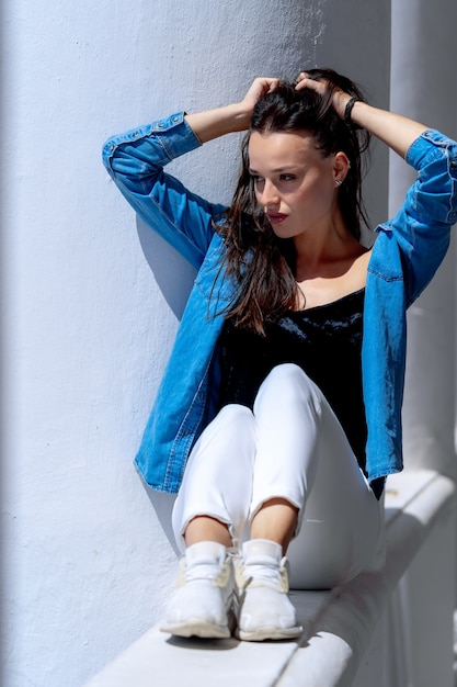 Ragazza seduta sul davanzale. Mani sui capelli sopra la testa. Ritratto a figura intera. Foto in stile casual.