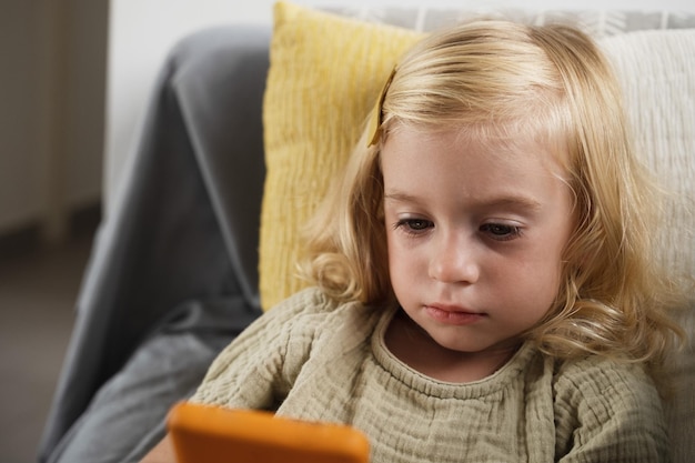 Ragazza seduta sul divano che guarda lo smartphone a casa bambino che gioca a cartoni animati di gamewatching