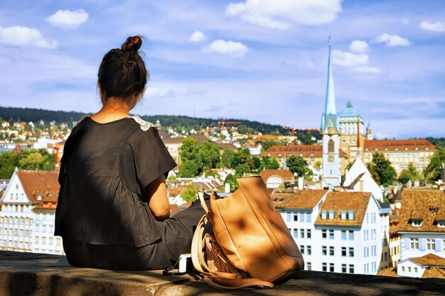 Ragazza seduta sulla collina di Lindenhof e guardando a Zurigo, Svizzera. Limmatquai e Predigerkirche sullo sfondo.