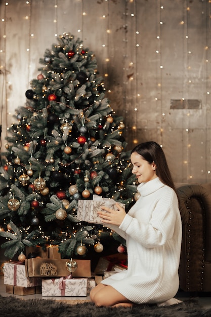 Ragazza seduta vicino all'albero di Natale e tenere un regalo di Natale.