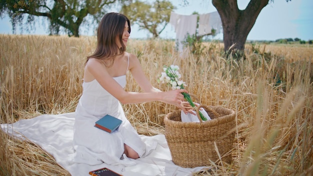 Ragazza sensuale che annusa fiori a un picnic estivo donna che prende un bouquet dal cesto