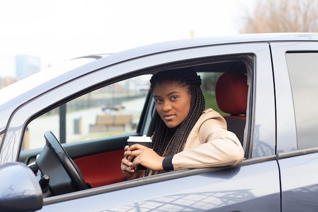 Ragazza seria che guida un'auto che beve caffè, afroamericano