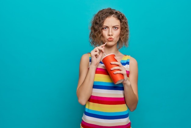 Ragazza seria con i capelli corti ricci che beve acqua fredda