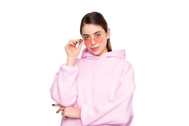 Ragazza seria in felpa con cappuccio rosa casual che regola gli occhiali isolati su bianco moda