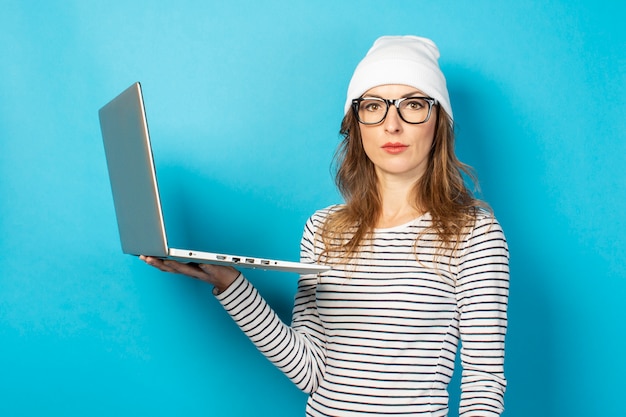 Ragazza seria in un cappello bianco con un computer portatile su un blu