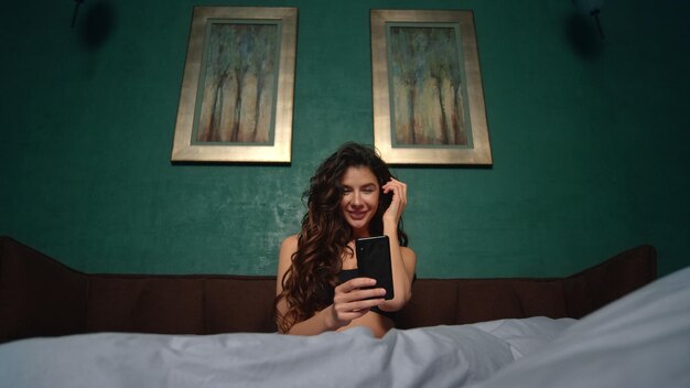 Ragazza sexy che prende il letto del telefono cellulare del selfie Bella donna che usa il telefono in camera da letto