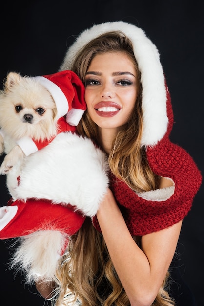 Ragazza sexy di babbo natale bella donna in costume da babbo natale con spitz di Pomerania capodanno dell'inverno del cane