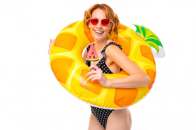 Ragazza sexy in un costume da bagno in un cerchio di nuoto sotto forma di ananas in vacanza su un bianco