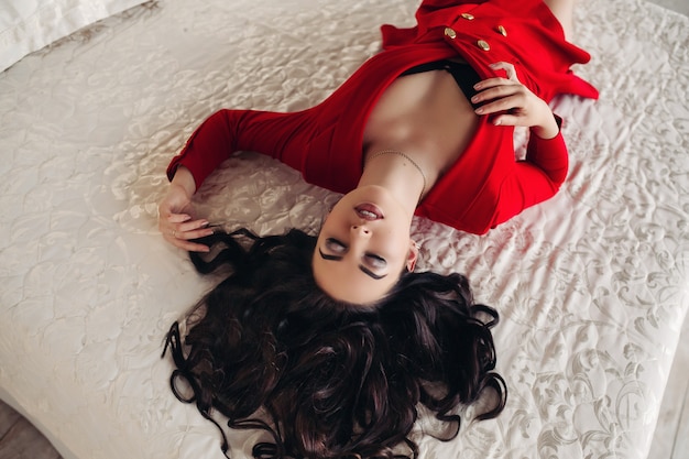 Ragazza sexy in vestito rosso che si trova sul letto con gli occhi chiusi.