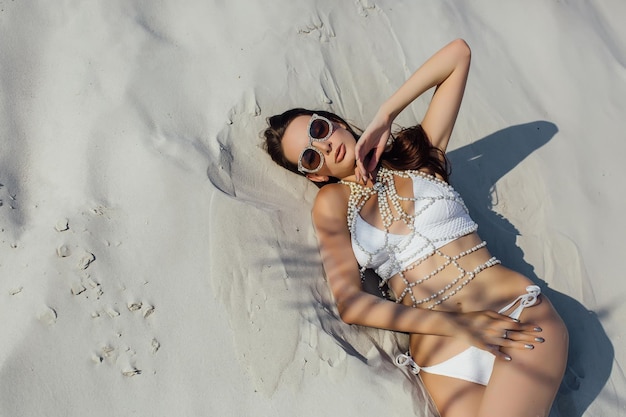 Ragazza sexy nella sabbia in un bikini bianco