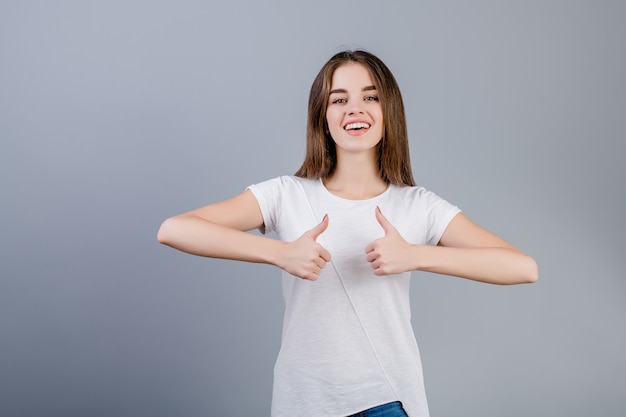 Ragazza smling felice che mostra i pollici in su isolati sopra grey