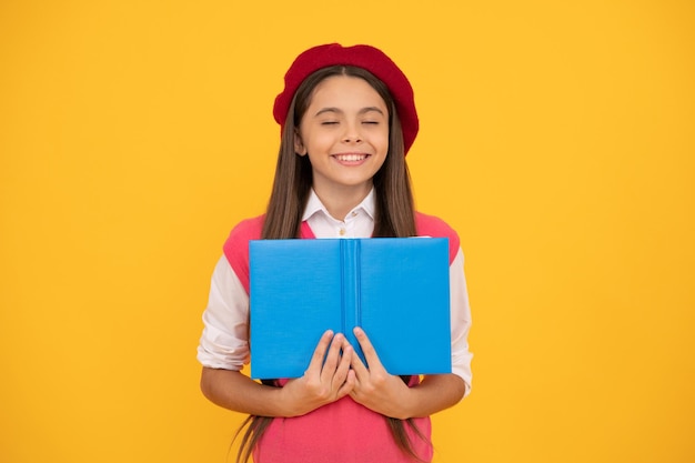 Ragazza sognante della scuola teenager nel libro di lettura del berretto francese su fondo giallo immagina