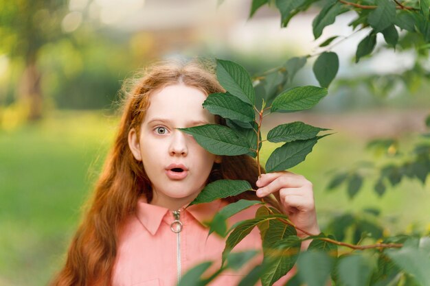 Ragazza sorpresa che tiene un ramo con foglie verdi vicino al viso