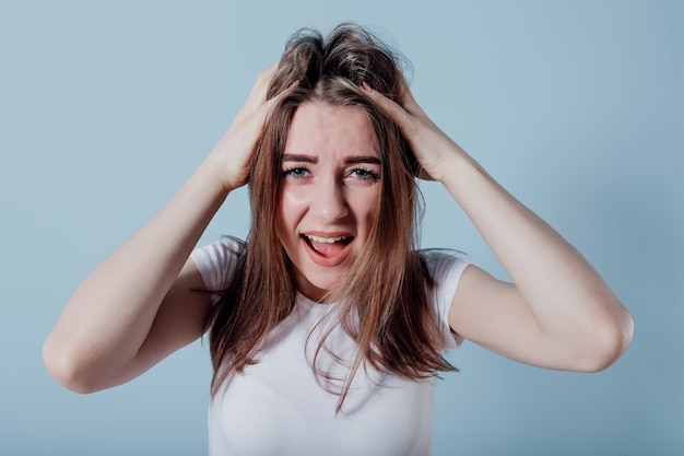 Ragazza sorpresa con le mani sulla testa. isolato sulla parete blu