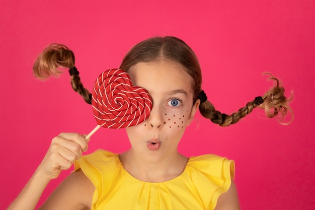 Ragazza sorpresa con lecca-lecca contro il muro rosa