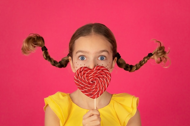 Ragazza sorpresa con lecca-lecca contro il muro rosa