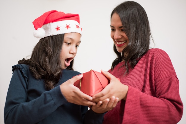 Ragazza sorpresa ed emozionata con il cappello di natale che riceve un regalo da sua madre.