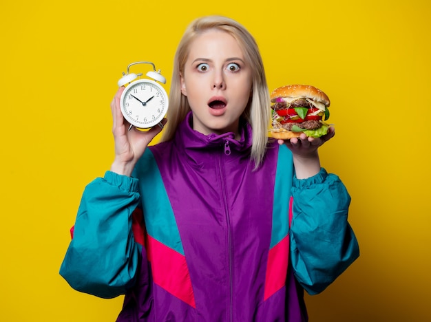 Ragazza sorpresa in stile anni '80 con hamburger e sveglia