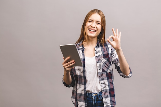 Ragazza sorridente attraente in casuale facendo uso della compressa che mostra segno giusto. Donna con tablet pc